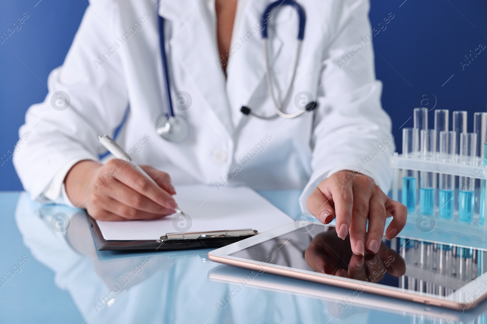 Photo of Doctor with tablet at table against blue background, closeup view