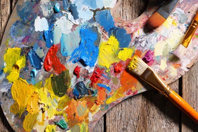 Photo of Artist's palette, brushes and paints on wooden table, flat lay