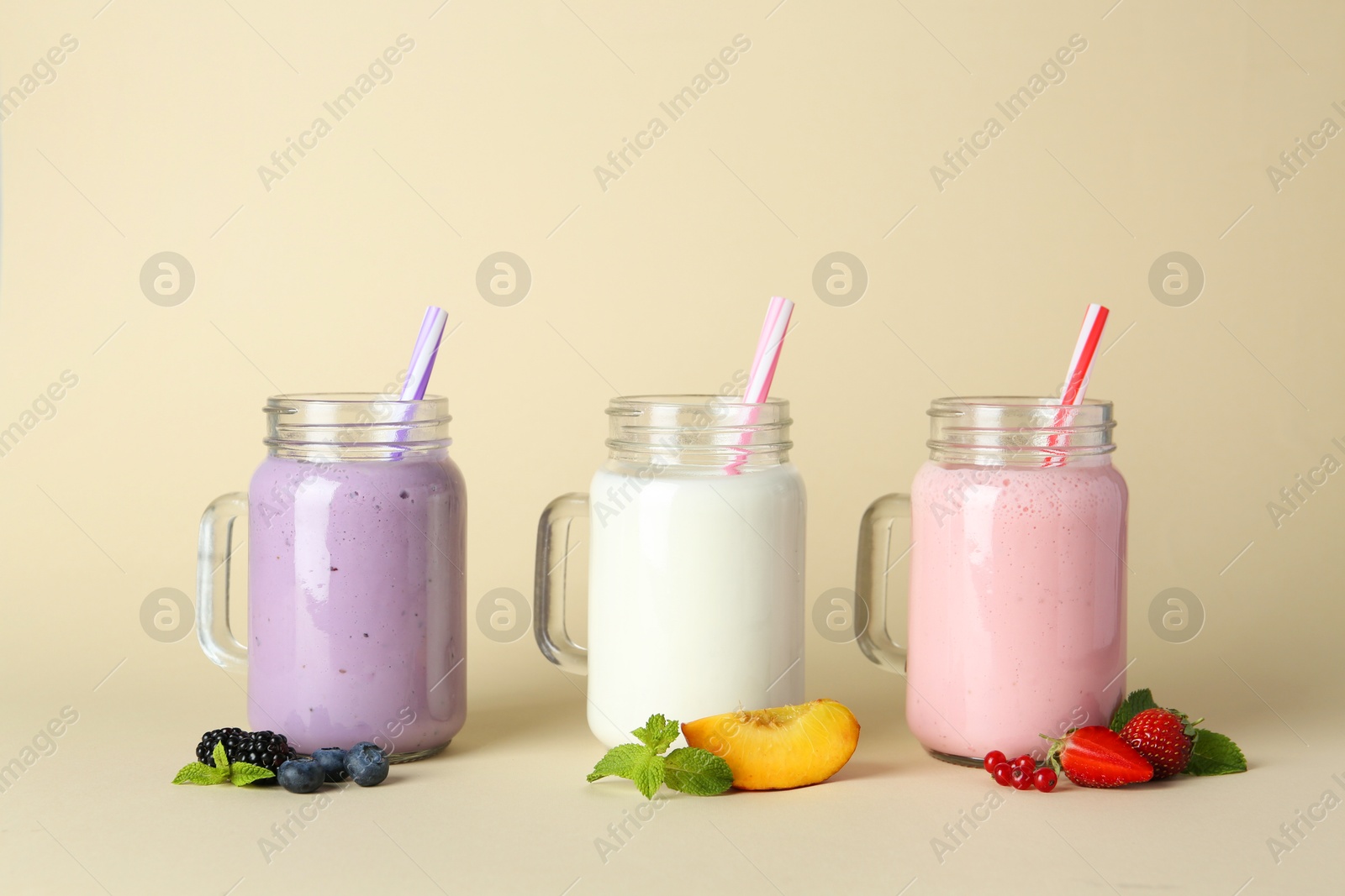 Photo of Different tasty yogurts in mason jars, peach, fresh berries and mint on pale yellow background