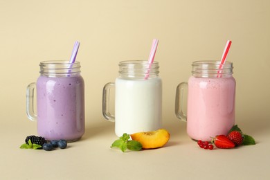 Photo of Different tasty yogurts in mason jars, peach, fresh berries and mint on pale yellow background