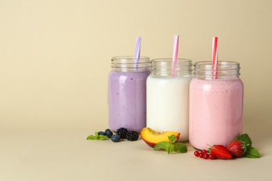 Photo of Different tasty yogurts in mason jars, peach, fresh berries and mint on pale yellow background, space for text