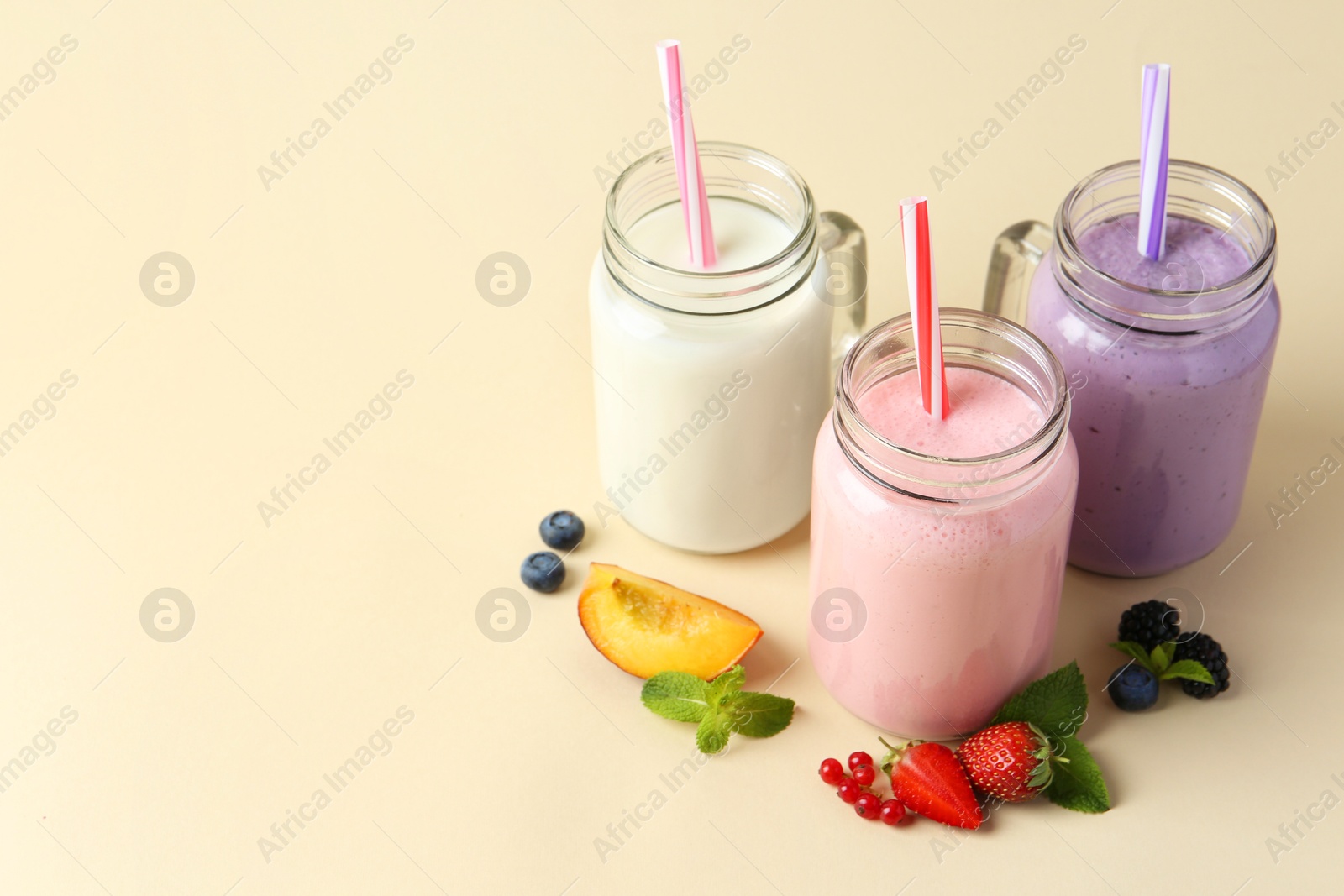 Photo of Different tasty yogurts in mason jars, peach, fresh berries and mint on pale yellow background, space for text