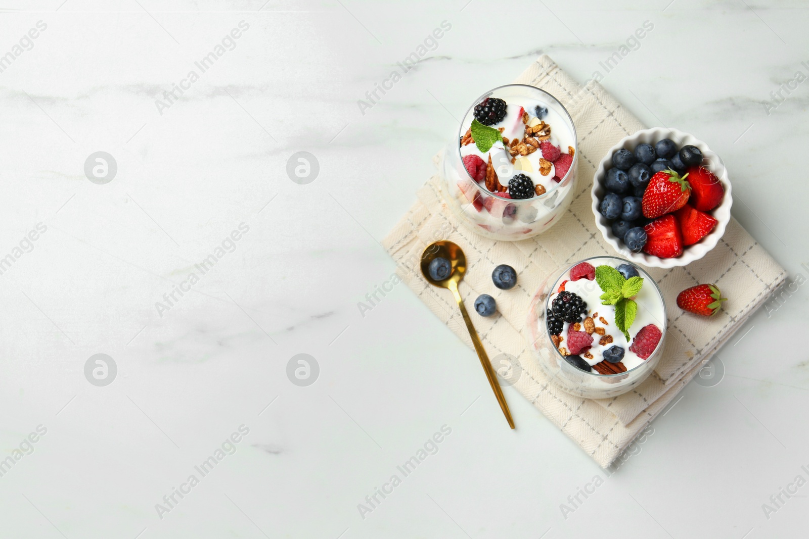 Photo of Tasty yogurt with fresh berries, granola and mint in glasses served on white table, flat lay. Space for text