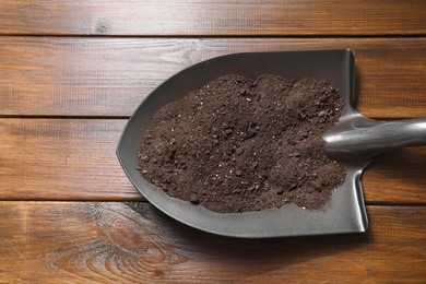 Photo of Metal shovel with soil on wooden table, top view