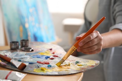 Woman with brush using palette at table indoors, closeup