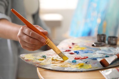 Woman with brush using palette at table indoors, closeup