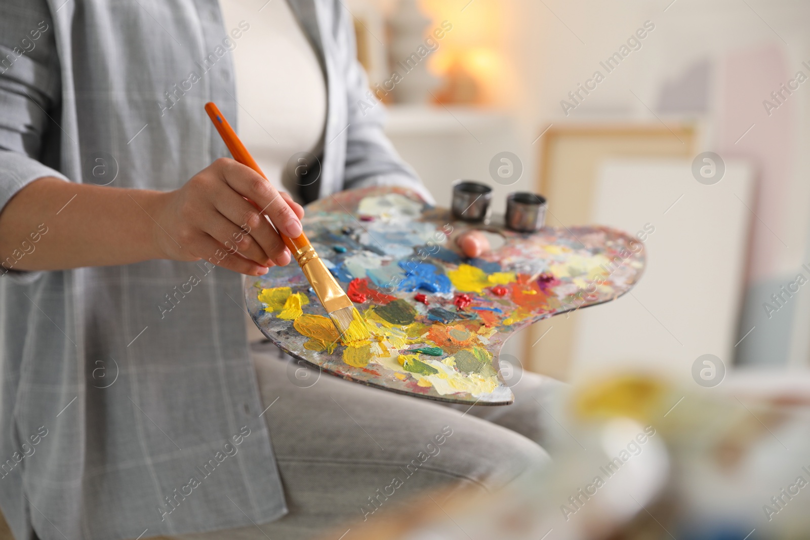 Photo of Woman with brush using palette near easel indoors, closeup