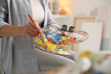 Woman with brush using palette near easel indoors, closeup