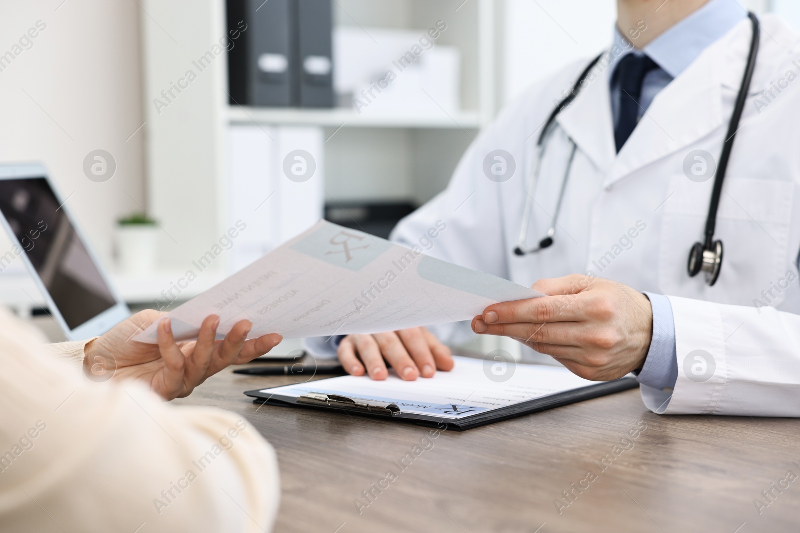 Photo of Doctor giving prescription to patient at wooden table in clinic, closeup