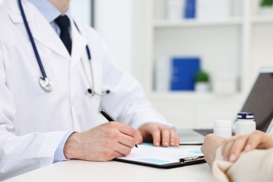 Photo of Doctor writing prescription for patient at white table in clinic, closeup