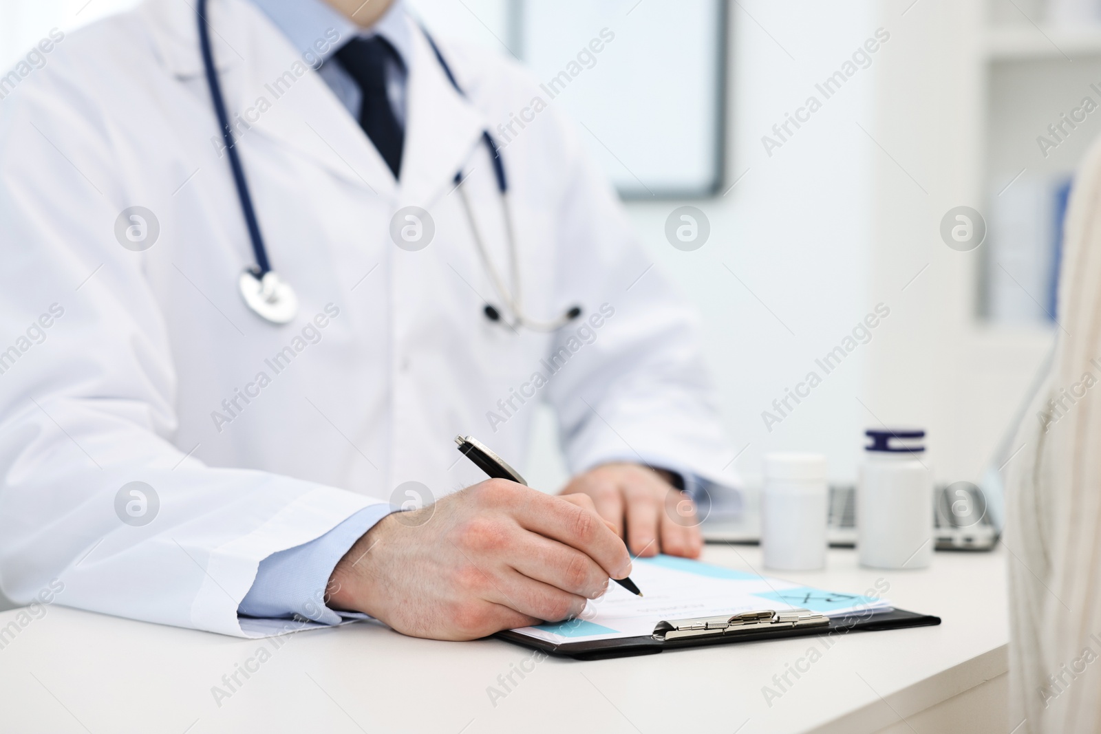 Photo of Doctor writing prescription for patient at white table in clinic, closeup