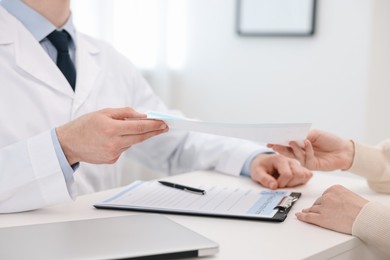 Photo of Doctor giving prescription to patient at white table in clinic, closeup