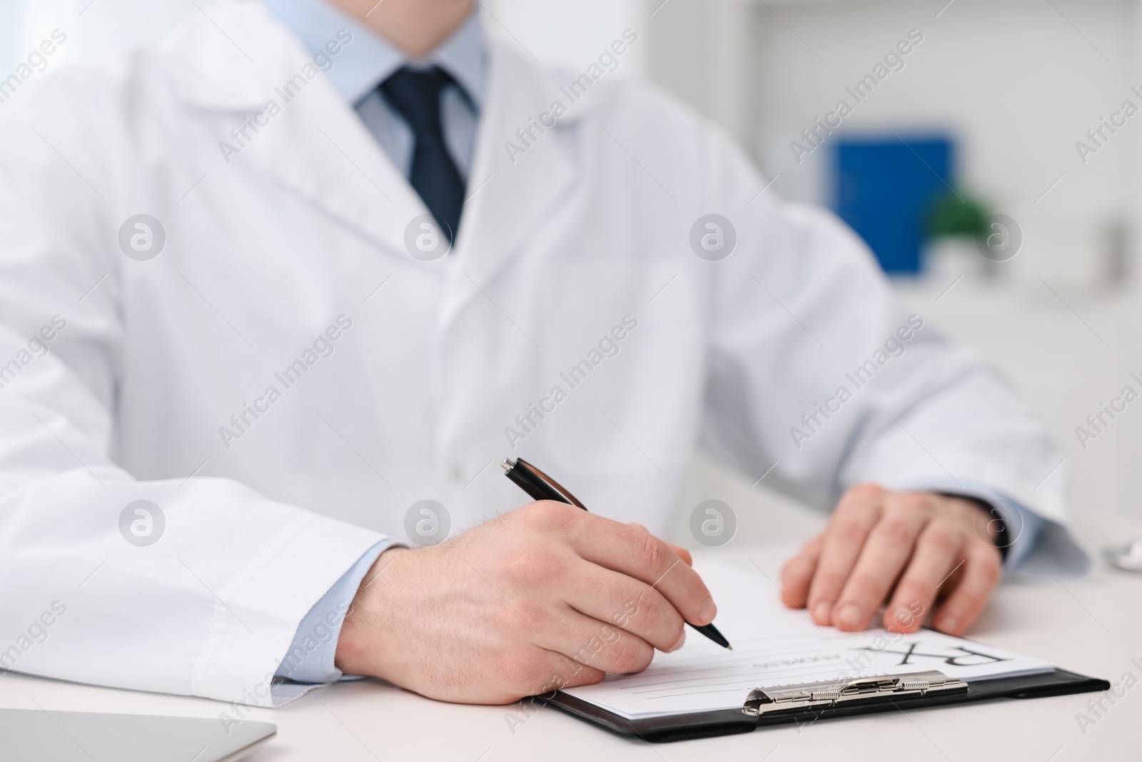 Photo of Doctor writing prescription at white table in clinic, closeup