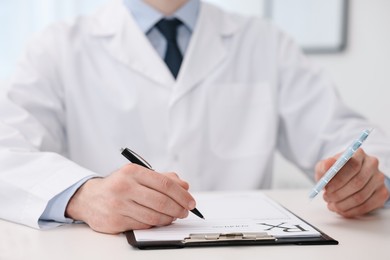 Photo of Doctor with pills writing prescription at white table in clinic, closeup