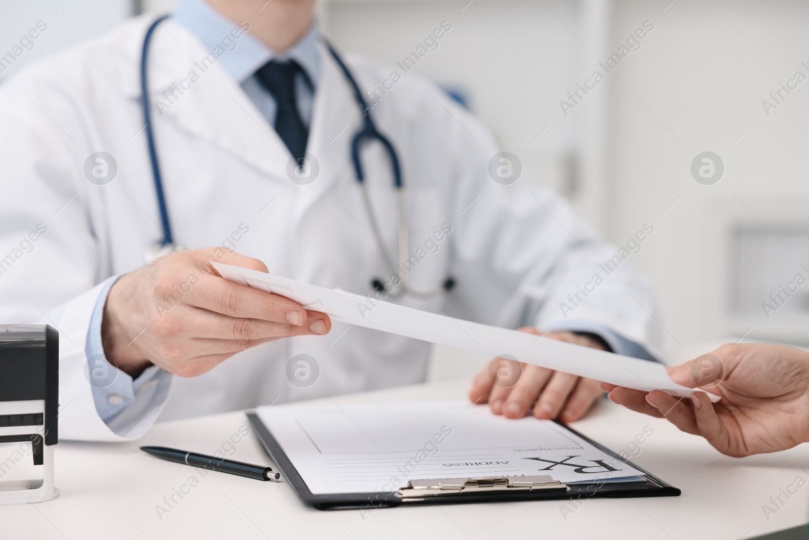 Photo of Doctor giving prescription to patient at white table in clinic, closeup