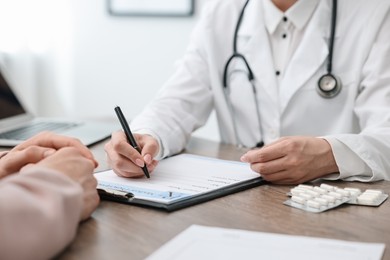 Photo of Doctor writing prescription for patient at wooden table in clinic, closeup