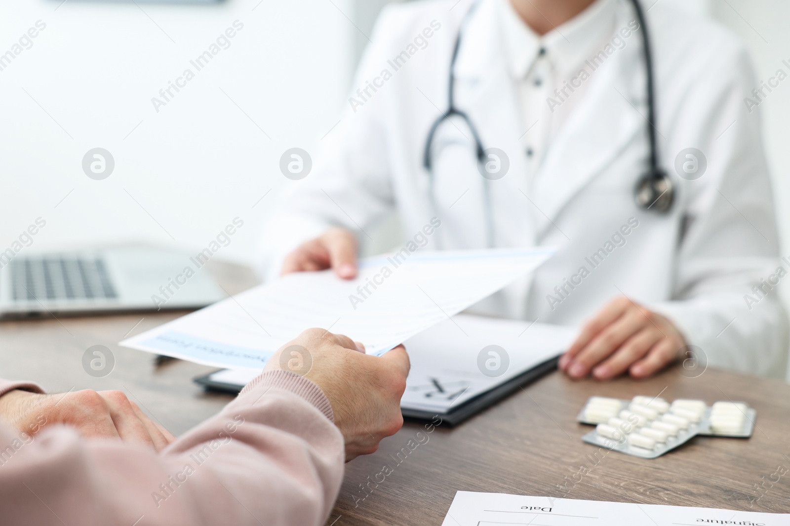 Photo of Doctor giving prescription to patient at wooden table in clinic, closeup