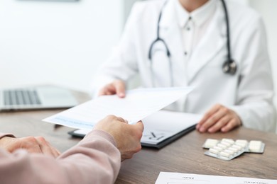 Photo of Doctor giving prescription to patient at wooden table in clinic, closeup