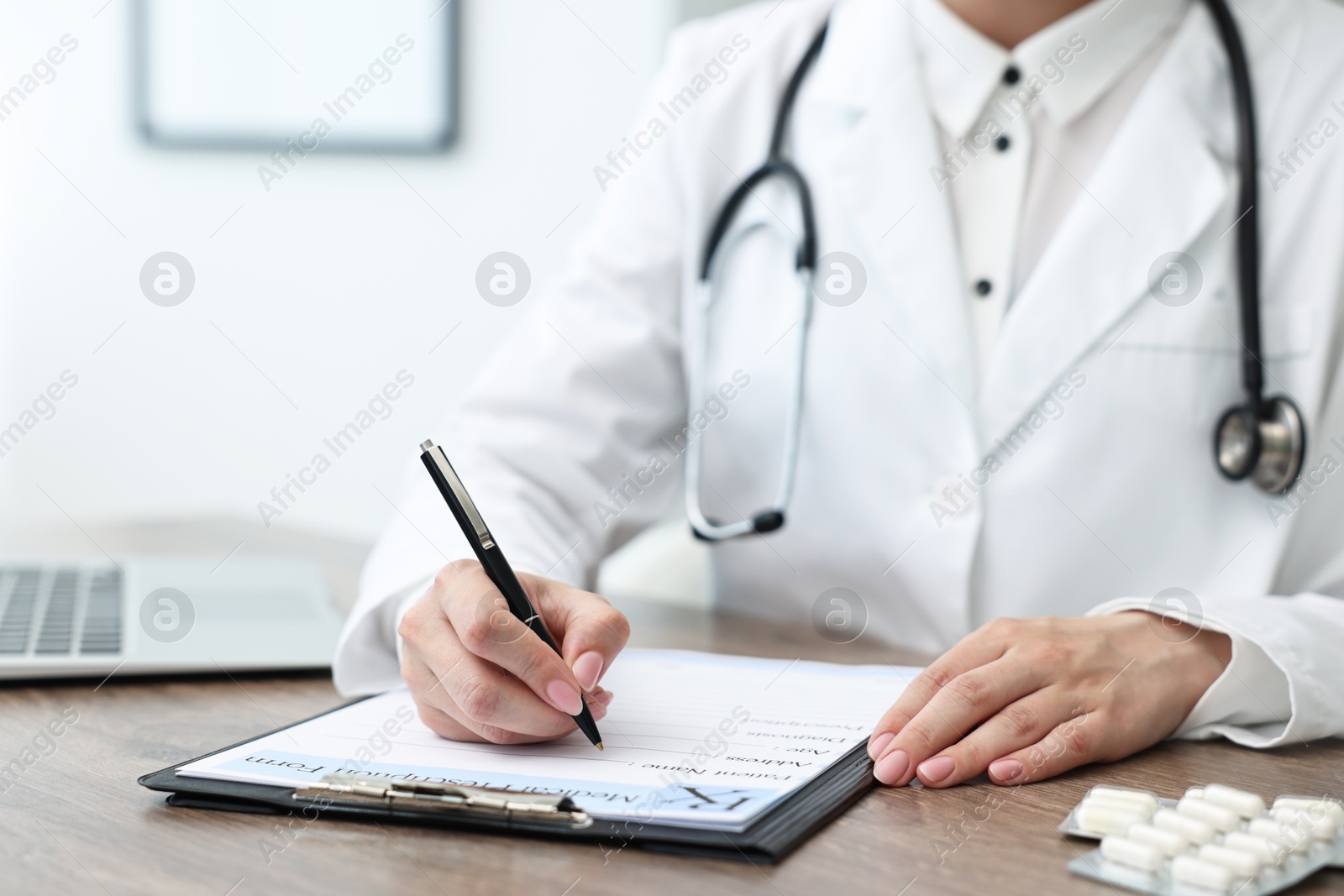 Photo of Doctor writing prescription at wooden table in clinic, closeup