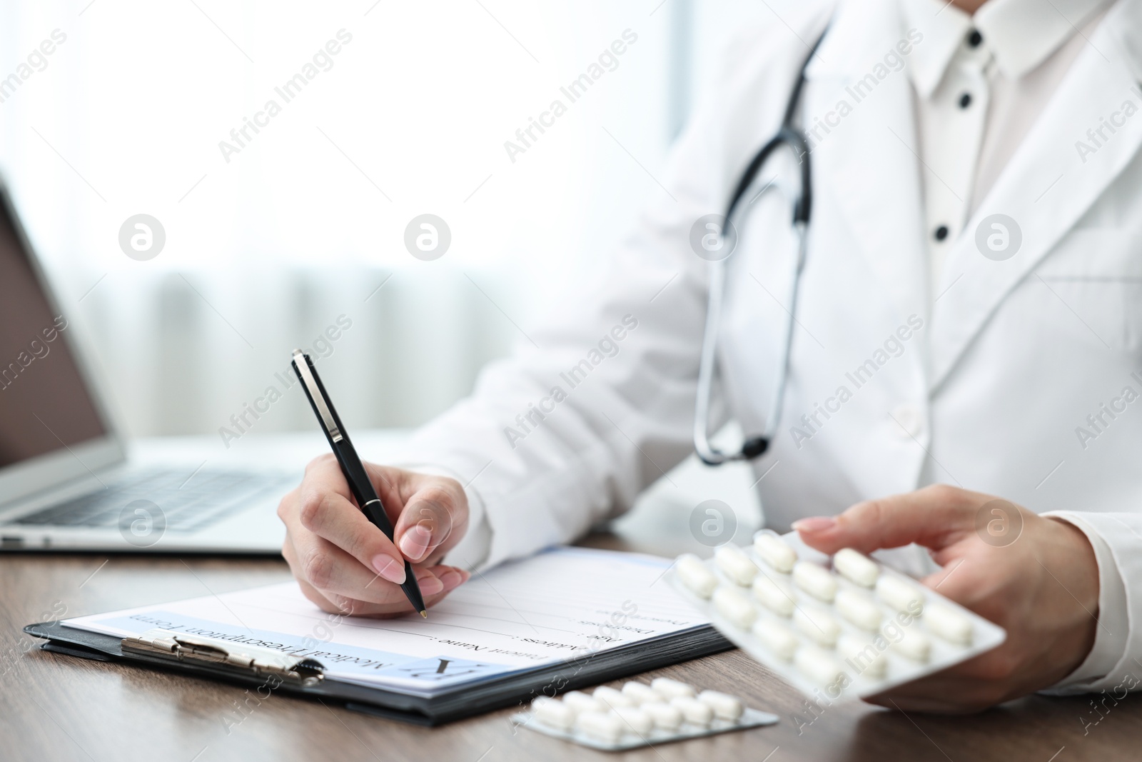 Photo of Doctor with pills writing prescription at wooden table in clinic, closeup