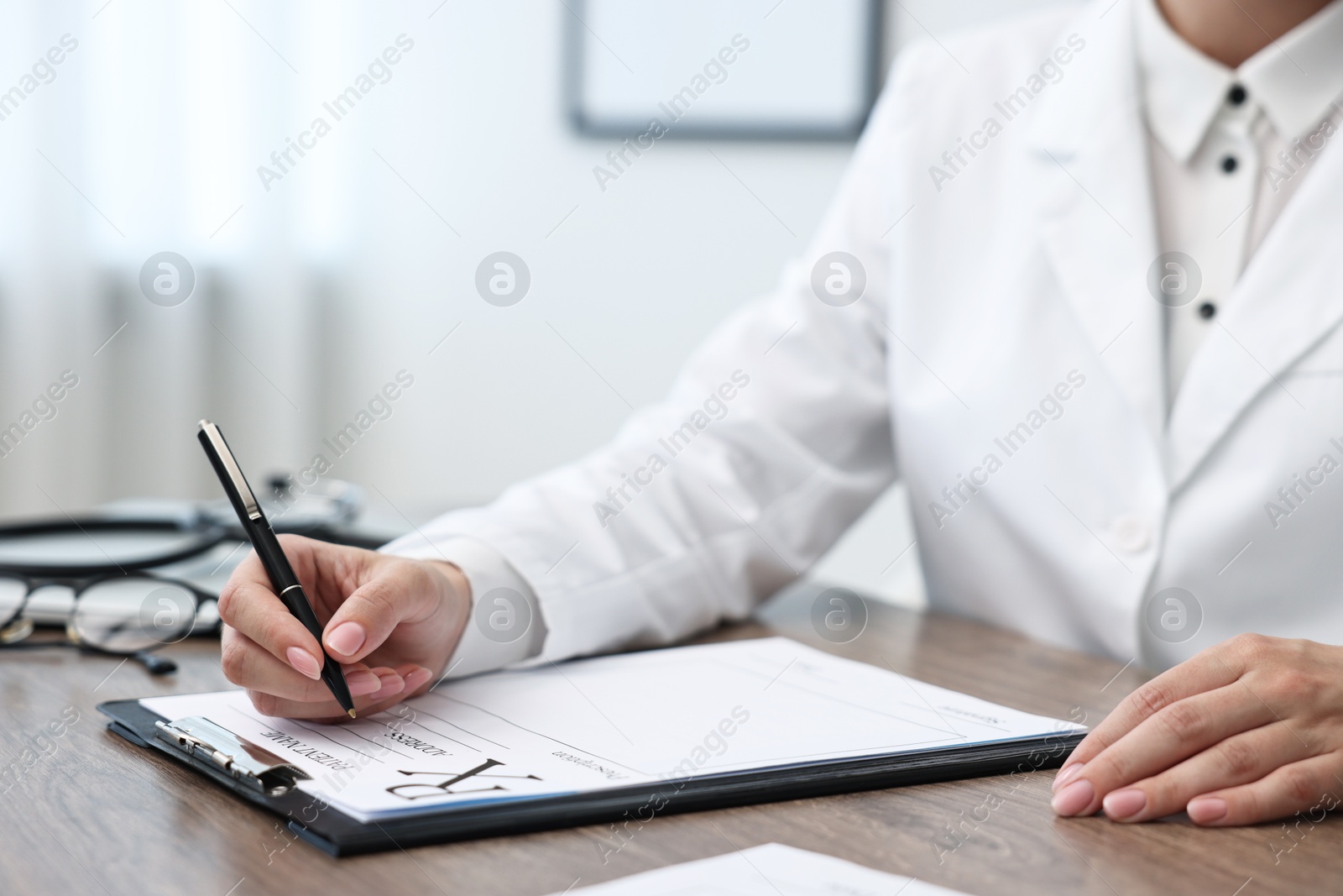 Photo of Doctor writing prescription at wooden table in clinic, closeup