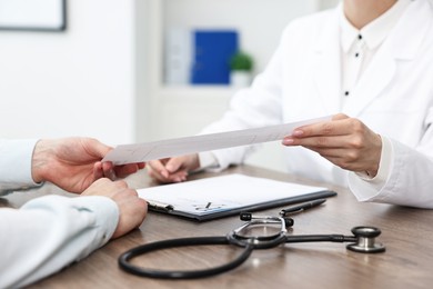 Photo of Doctor giving prescription to patient at wooden table in clinic, closeup