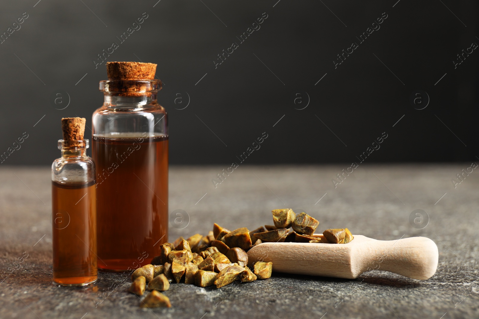 Photo of Honey tincture and scoop with propolis granules on grey textured table, closeup. Space for text