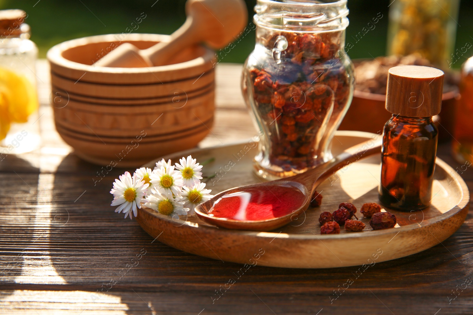 Photo of Tincture, chamomiles, dried berries, mortar and pestle on wooden table outdoors