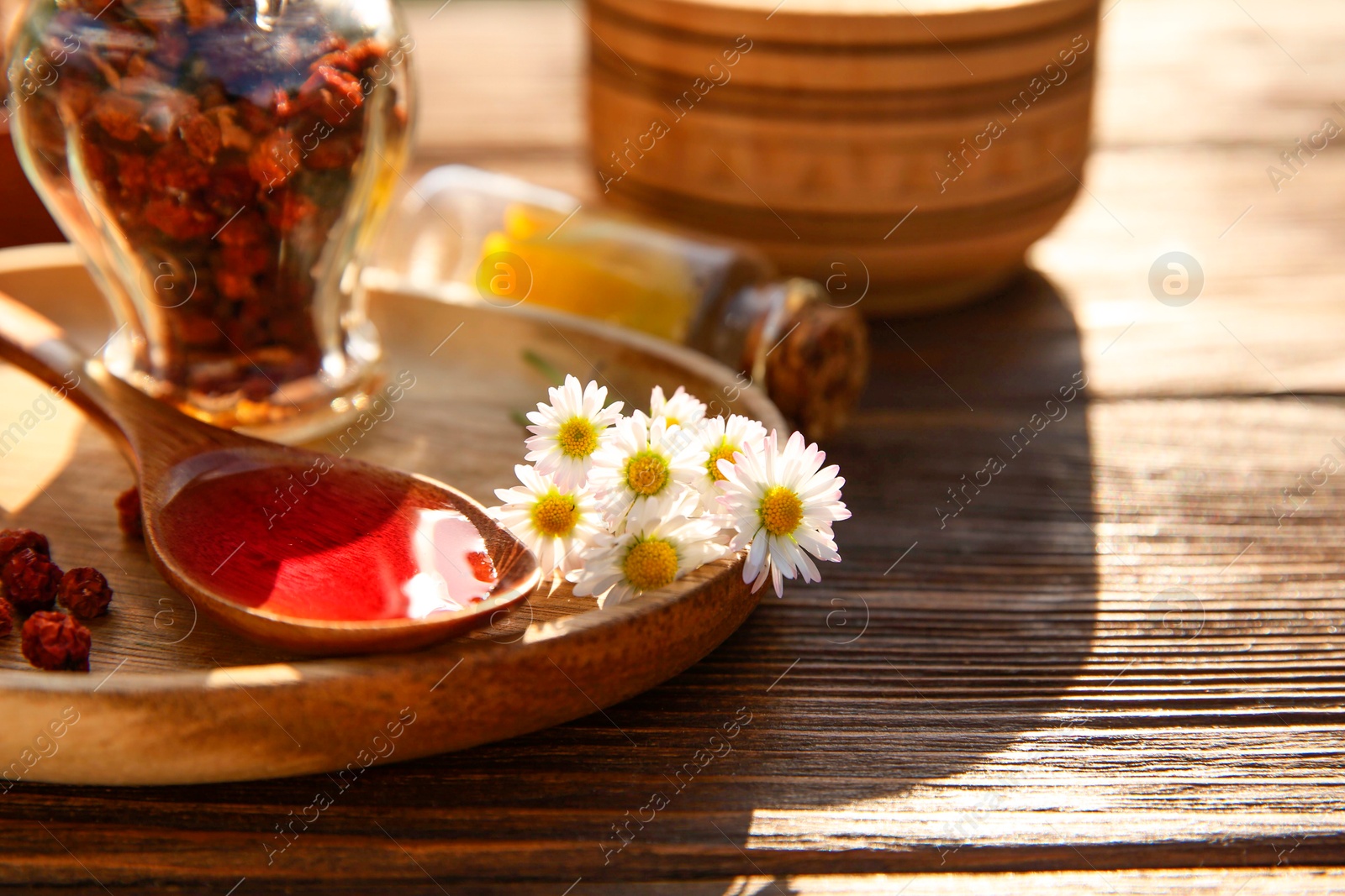 Photo of Tincture in spoon, chamomiles and dried berries on wooden table