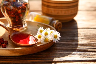 Tincture in spoon, chamomiles and dried berries on wooden table