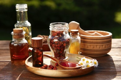 Different tinctures, ingredients, mortar and pestle on wooden table outdoors