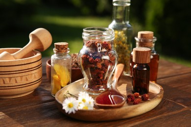 Different tinctures, ingredients, mortar and pestle on wooden table outdoors