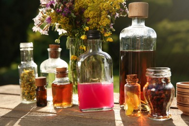 Different tinctures in bottles and ingredients on wooden table outdoors