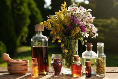 Different tinctures in bottles, ingredients, mortar and pestle on wooden table outdoors