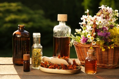 Photo of Tincture in bottles and different flowers on wooden table outdoors