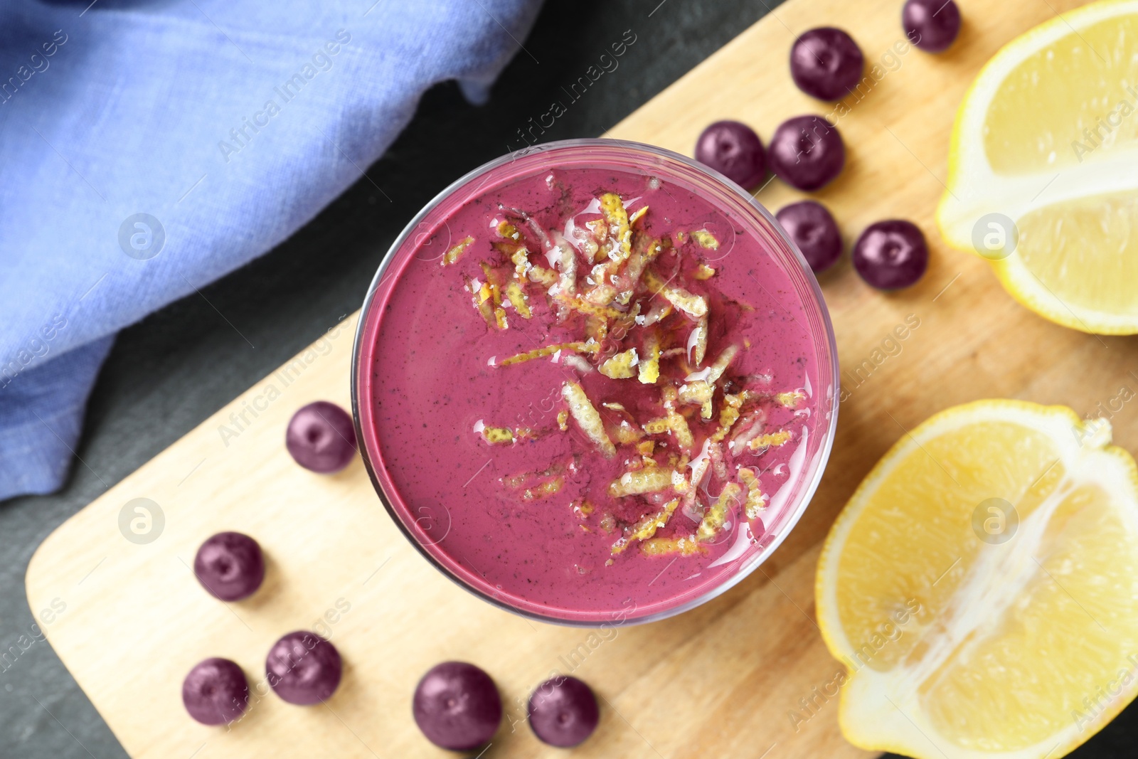 Photo of Tasty fresh acai juice in glass with berries and lemon on grey table, flat lay