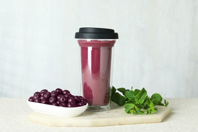 Tasty fresh acai juice in glass, mint and berries on light textured table