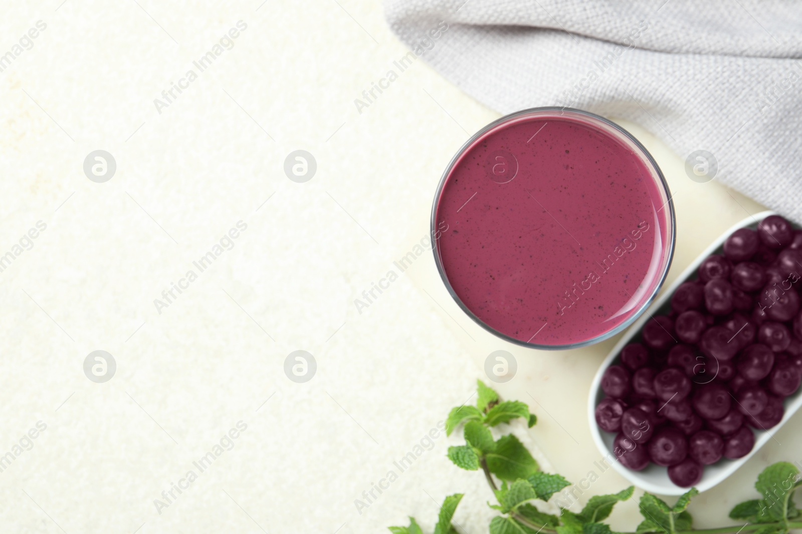 Photo of Tasty fresh acai juice in glass with mint and berries on light table, flat lay. Space for text