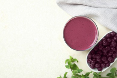 Photo of Tasty fresh acai juice in glass with mint and berries on light table, flat lay. Space for text