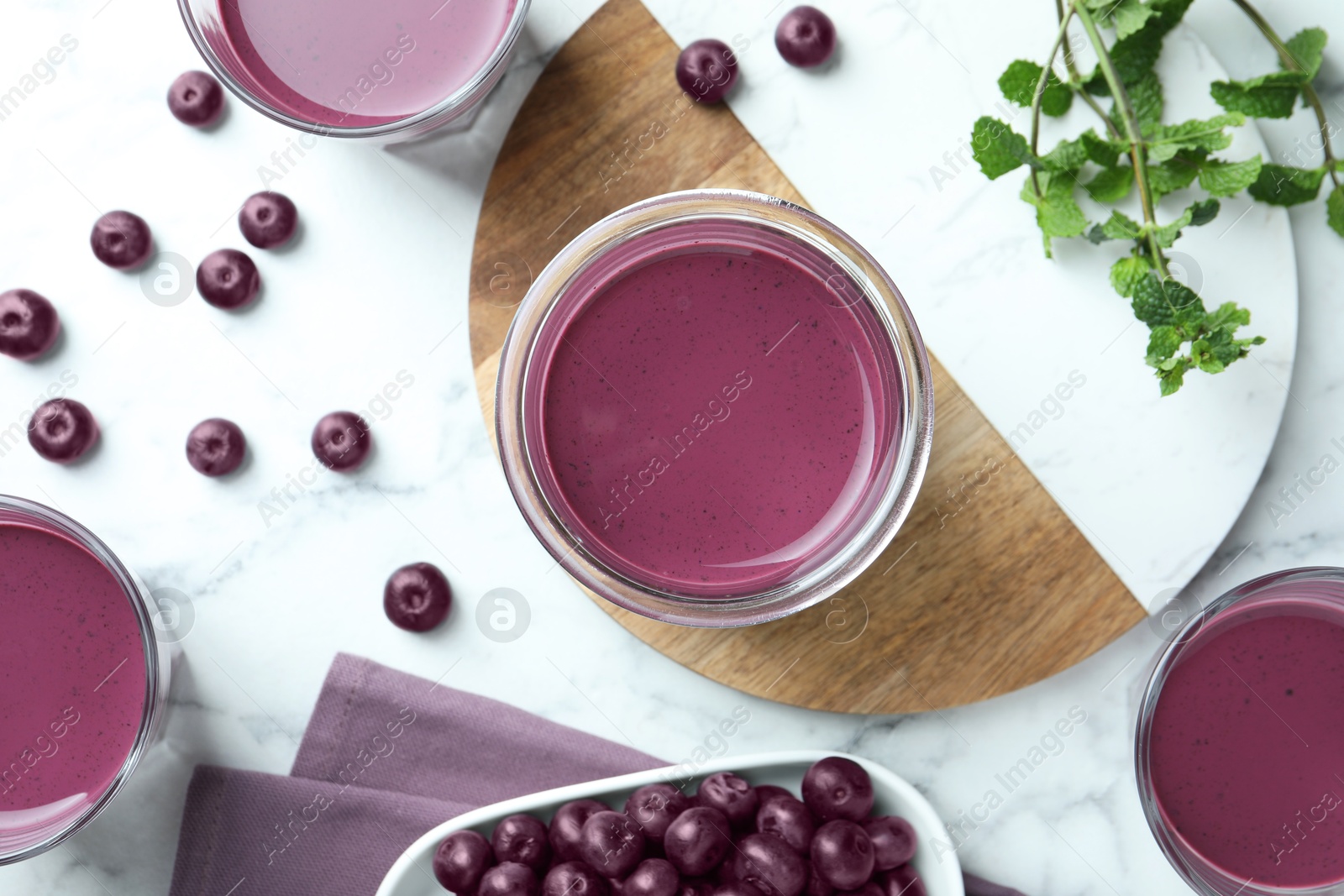 Photo of Tasty fresh acai juice in glasses, mint and berries on white marble table, flat lay