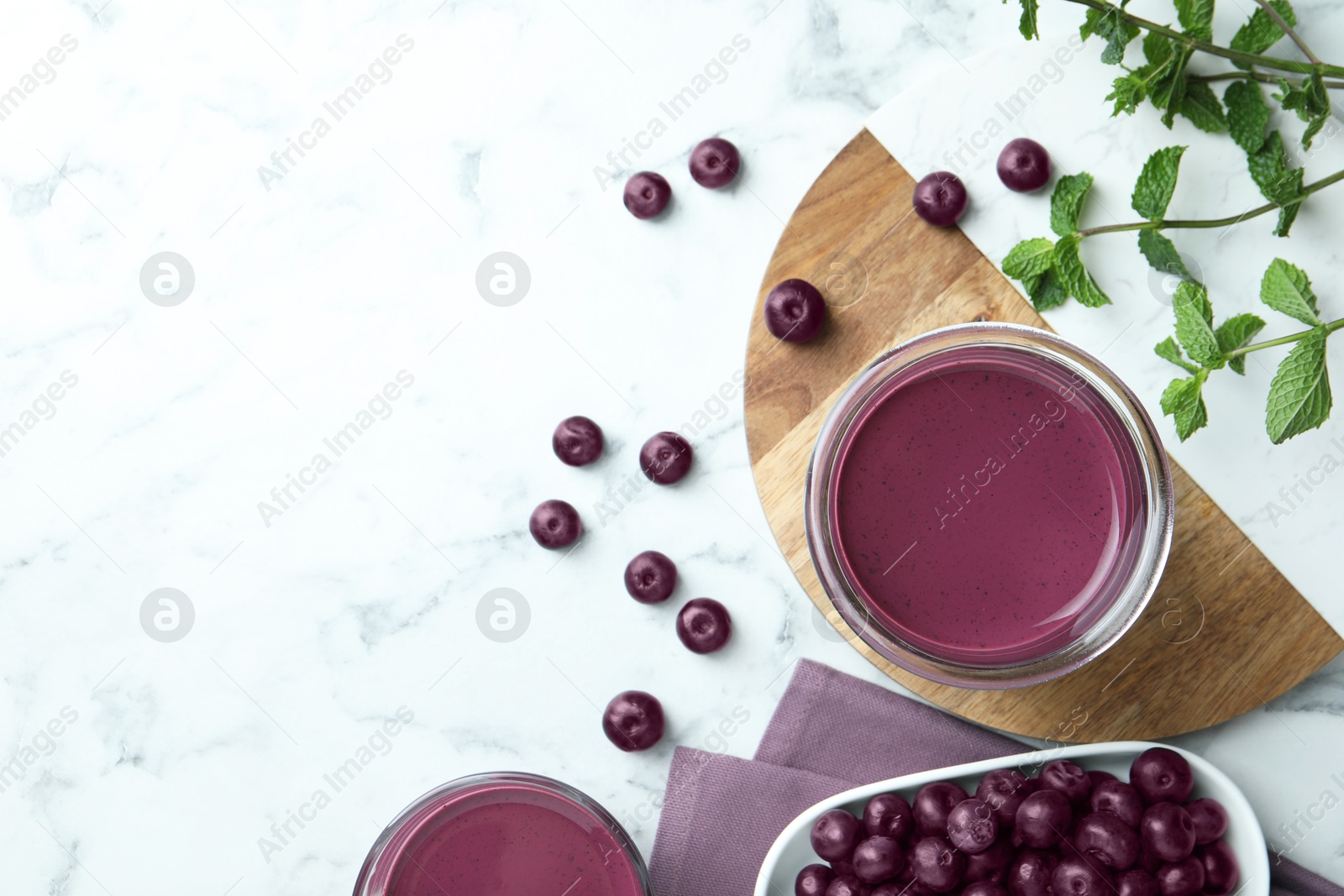 Photo of Tasty fresh acai juice in glasses, mint and berries on white marble table, flat lay. Space for text