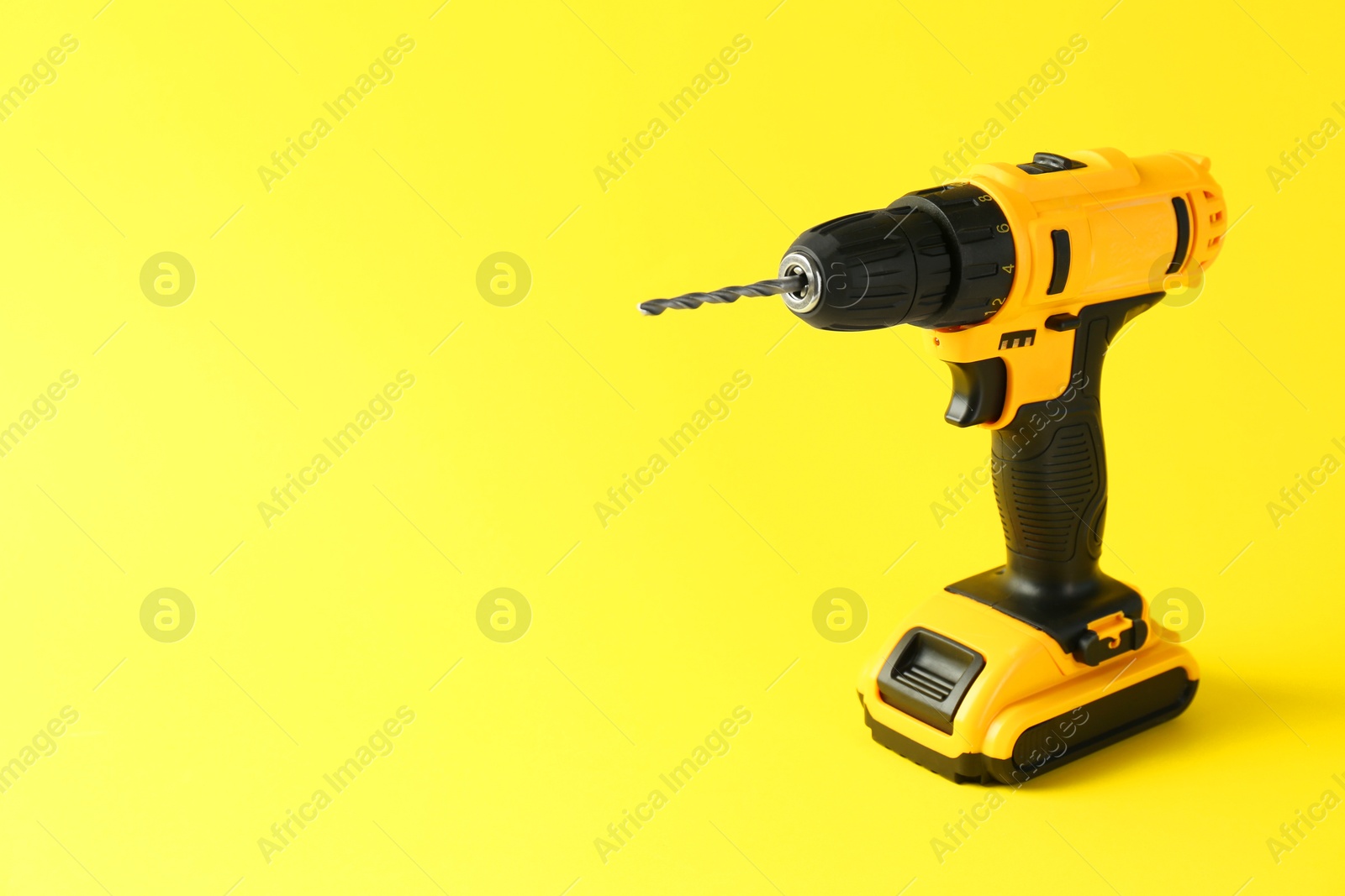 Photo of Modern cordless electric drill on yellow background. Space for text