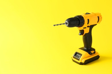 Modern cordless electric drill on yellow background. Space for text