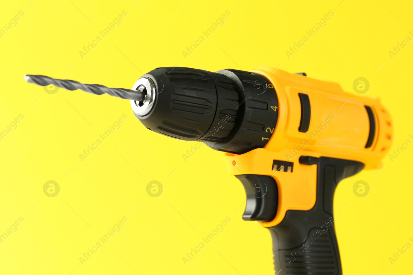 Photo of Modern cordless electric drill on yellow background, closeup