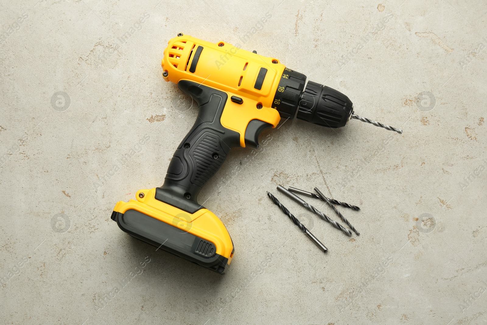 Photo of Modern cordless electric drill and bits on light grey table, top view