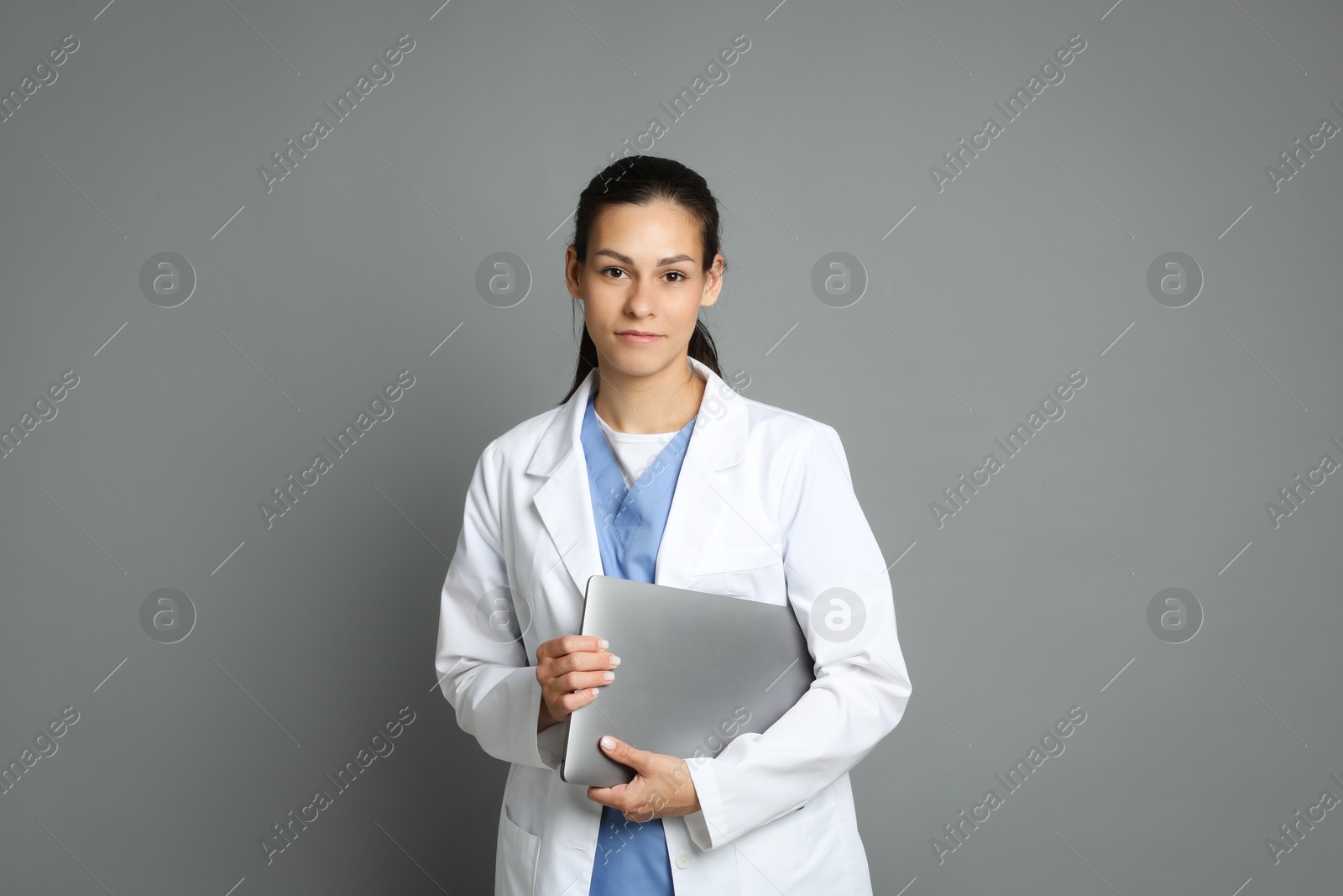 Photo of Portrait of beautiful nurse with laptop on grey background