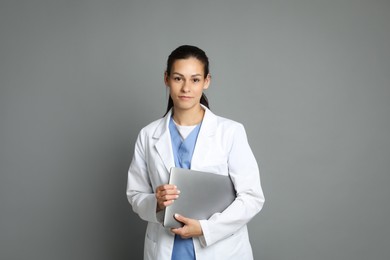 Portrait of beautiful nurse with laptop on grey background