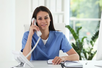 Photo of Smiling nurse working with clients by telephone at table in hospital office