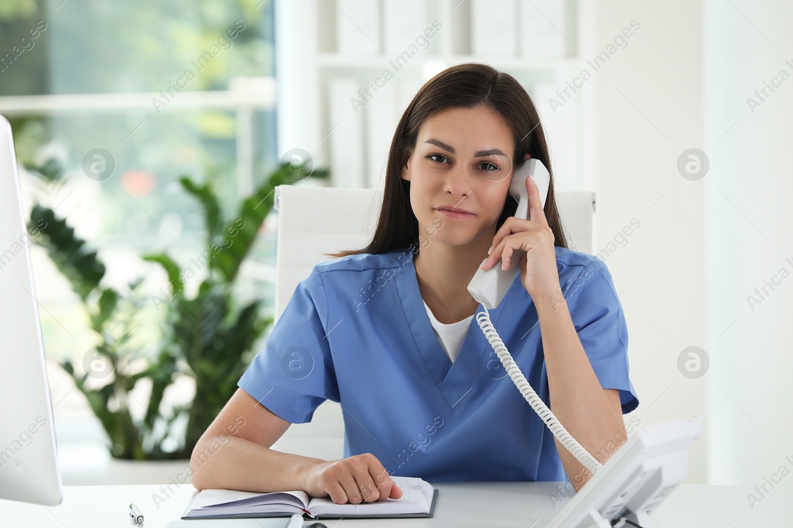 Photo of Beautiful nurse working with clients by telephone at table in hospital office