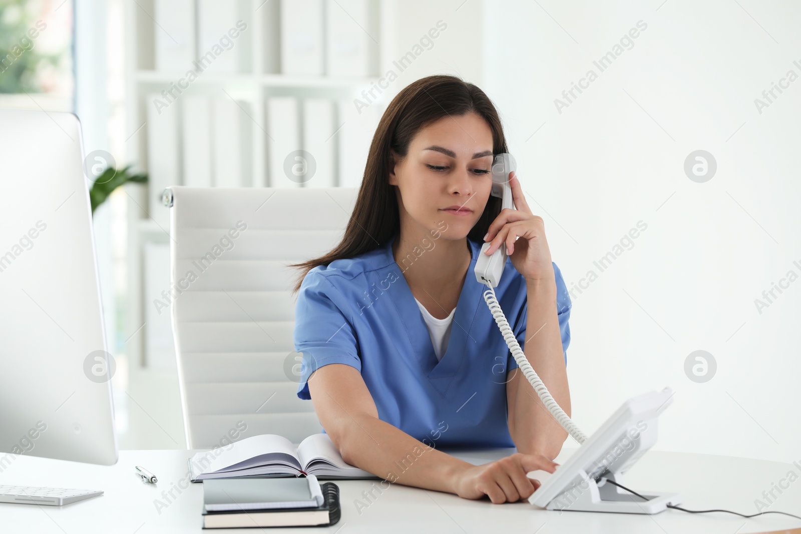 Photo of Beautiful nurse working with clients by telephone at table in hospital office